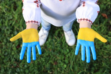 Photo of Little girl with hands painted in Ukrainian flag colors outdoors, top view. Love Ukraine concept