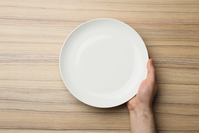 Man with empty plate at wooden table, top view