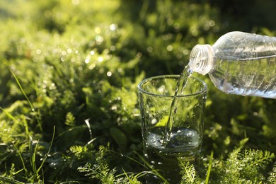 Photo of Pouring fresh water from bottle into glass on green grass outdoors. Space for text