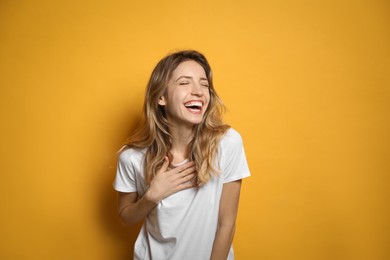 Cheerful young woman laughing on yellow background