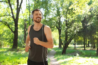 Handsome man with headphones running in park, space for text. Morning exercise