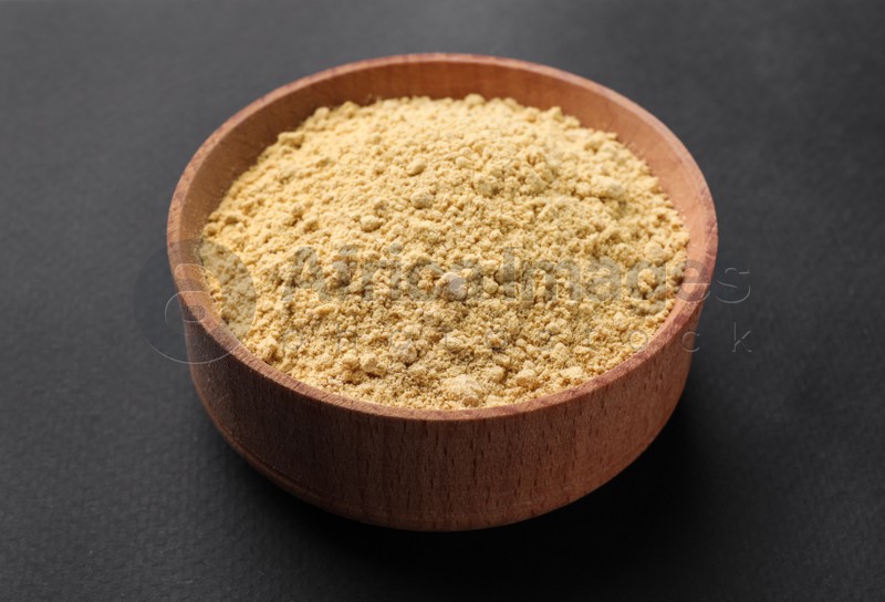 Photo of Aromatic mustard powder in wooden bowl on dark background