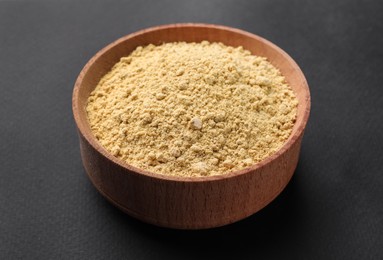 Aromatic mustard powder in wooden bowl on dark background
