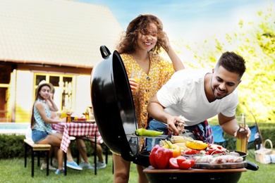 Young man and woman with drinks near barbecue grill outdoors