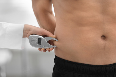 Nutritionist measuring man's body fat layer with digital caliper on blurred background, closeup