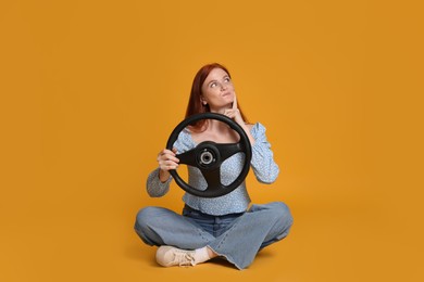 Young woman with steering wheel on yellow background