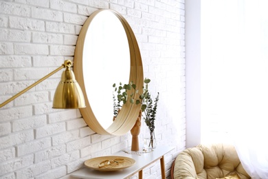 Big round mirror, table with jewelry and decor near brick wall in hallway interior. Space for text