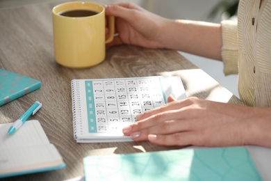 Woman with calendar and cup of drink at wooden table, closeup