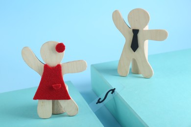 Gender pay gap. Wooden figures of man and woman on light blue background
