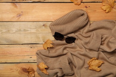 Photo of Warm sweater, sunglasses and dry leaves on wooden background, flat lay with space for text. Autumn season