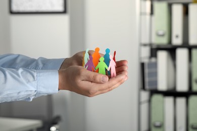 Photo of Man holding paper human figures in office, closeup. Diversity and Inclusion concept