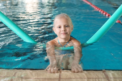 Little girl with swimming noodle in indoor pool