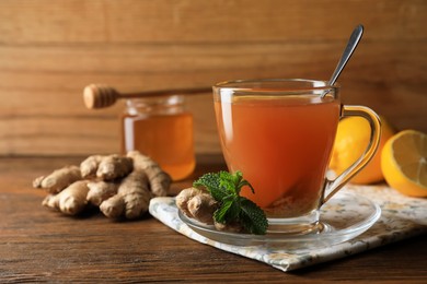 Photo of Cup of delicious ginger tea and ingredients on wooden table, space for text