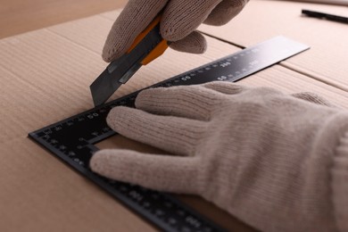 Worker cutting cardboard with utility knife and ruler, closeup