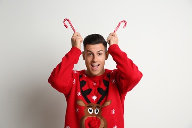 Photo of Funny man in Christmas sweater with candy canes on white background
