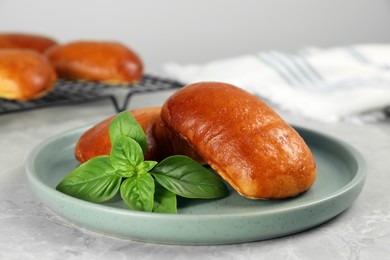 Photo of Delicious baked pirozhki and basil on light grey marble table, closeup