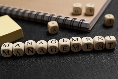 Word Management made of cubes near paper notes and notebook on black background, closeup