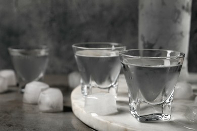 Shot glasses and bottle of vodka with ice cubes on light grey table, closeup