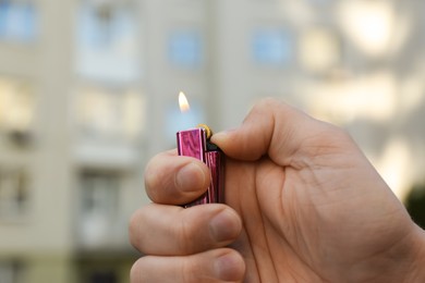 Photo of Man holding lighter with burning flame outdoors, closeup