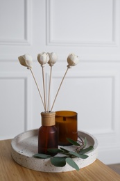 Reed air freshener with candle and eucalyptus branch on tray indoors