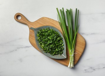 Chopped green spring onion and stems on white marble table, top view