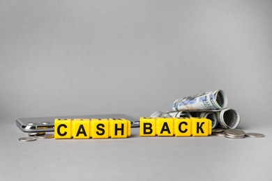 Word Cashback made with cubes, money and smartphone on grey background