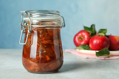 Tasty apple jam in glass jar and fresh fruits on light table, space for text