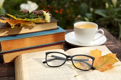 Photo of Yellow maple leaf, glasses, book and cup of tea on wooden table. Autumn atmosphere