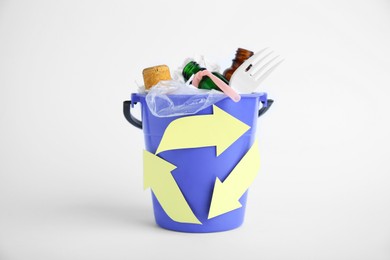 Bucket with recycling symbol full of garbage on white background