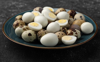 Photo of Peeled and unpeeled hard boiled quail eggs in plate on black table, closeup