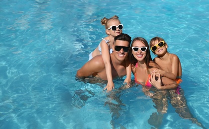 Happy family in outdoor swimming pool on sunny summer day. Space for text