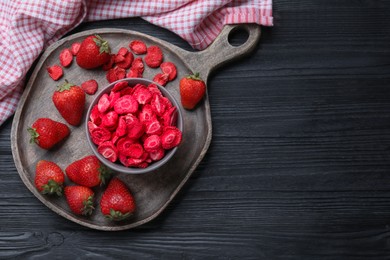 Photo of Freeze dried and fresh strawberries on black wooden table, top view. Space for text