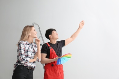 Male decorator and young woman choosing color for walls in empty room