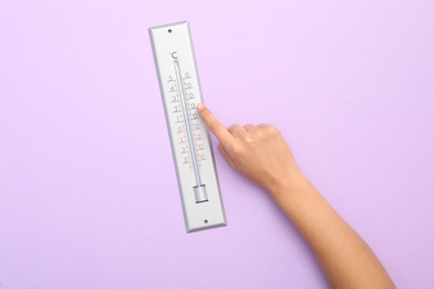 Woman with weather thermometer on lilac background, top view