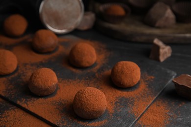 Delicious chocolate truffles powdered with cocoa on black table, closeup