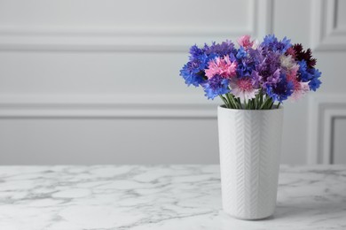 Bouquet of beautiful cornflowers in vase on white marble table. Space for text