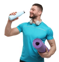 Photo of Handsome man with thermo bottle, fitness mat and headphones on white background