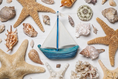 Flat lay composition with toy ship and sea shells on white wooden background
