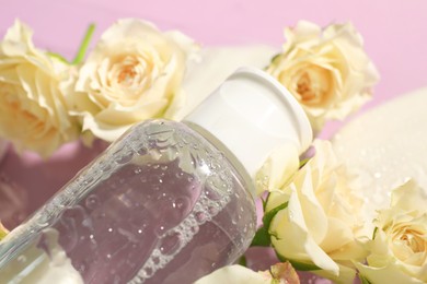Wet bottle of micellar water and beautiful white roses on pink background, closeup