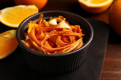 Photo of Bowl with dry orange peels and fresh fruits on wooden table, closeup
