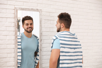 Young man looking at himself in large mirror at home