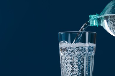 Photo of Pouring soda water from bottle into glass on blue background, closeup. Space for text