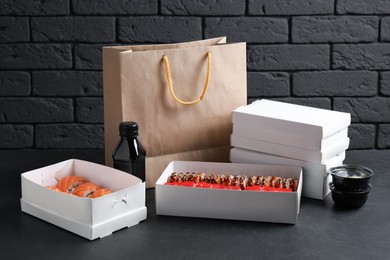 Food delivery. Boxes with delicious sushi rolls, paper package and soy sauce on black table