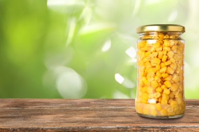 Jar of pickled corn on wooden table against blurred background, space for text