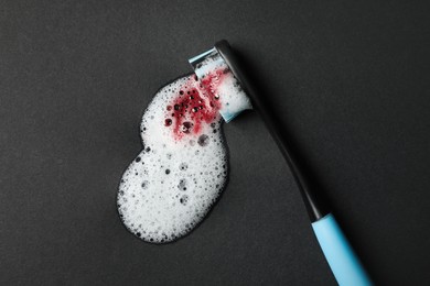 Toothbrush with paste and blood on black background, top view. Gum inflammation