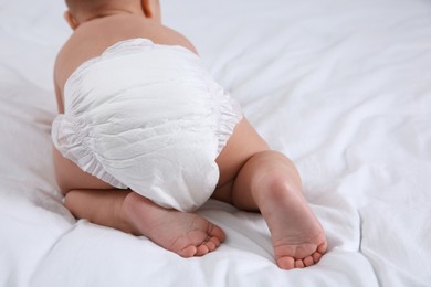 Cute baby in dry soft diaper on white bed, closeup