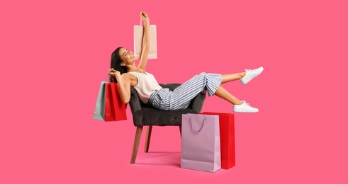 Beautiful young woman with paper shopping bags in armchair on pink background