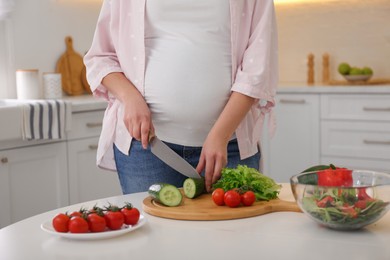 Young pregnant woman preparing vegetable salad at table in kitchen, closeup. Healthy eating