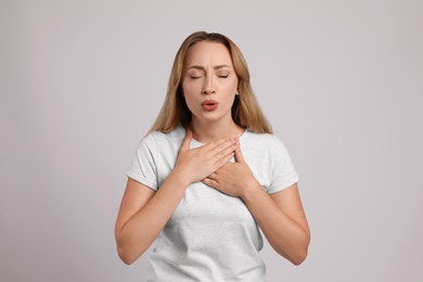 Young woman suffering from pain during breathing on light grey background