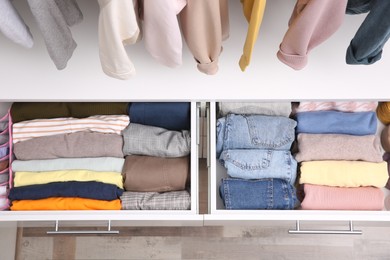 Photo of Open drawers with folded clothes indoors, top view. Vertical storage